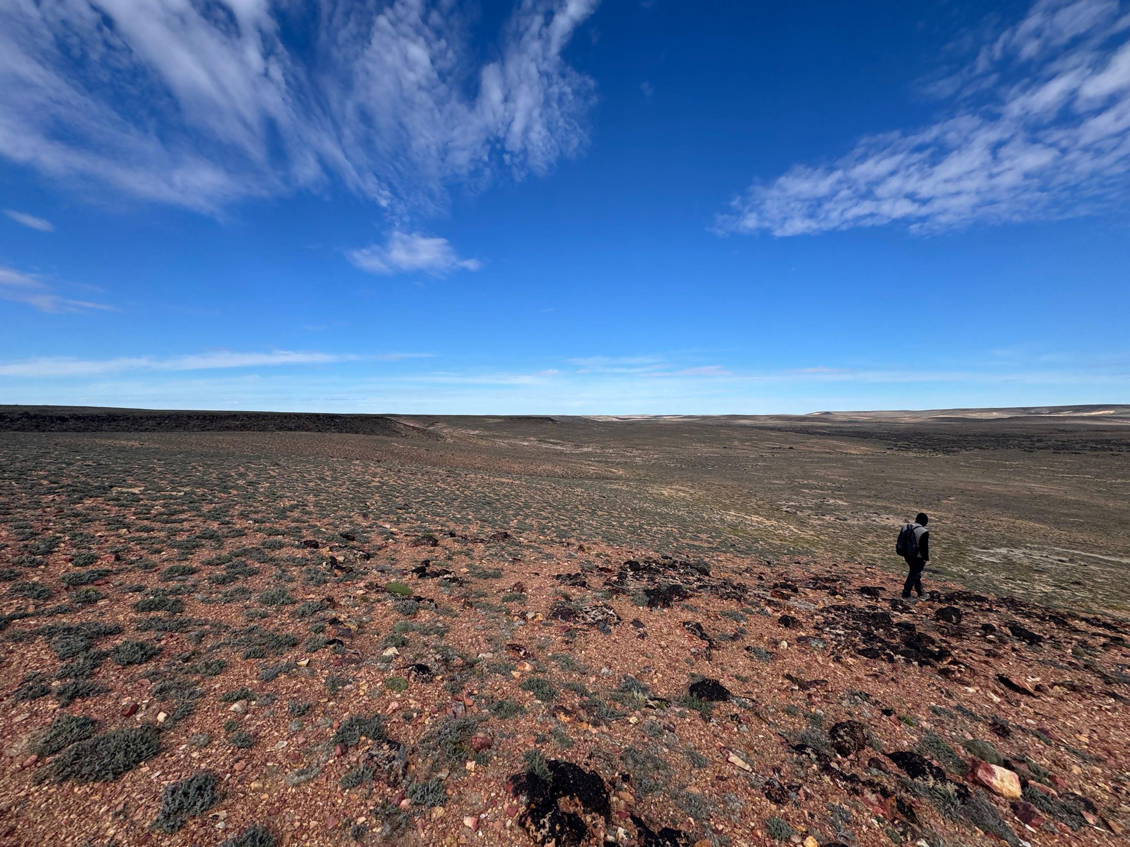 A geologist walking the red volcanic plateau of the Luna Roja project under a wide Patagonian sky